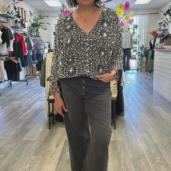 Lady wearing back & white V-neck blouse with buttons down the front, long sleeves and black denim.  Located inside of August Boutique