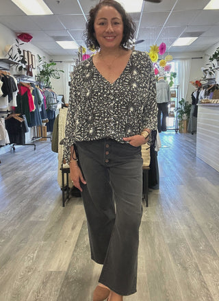 Lady wearing back & white V-neck blouse with buttons down the front, long sleeves and black denim.  Located inside of August Boutique